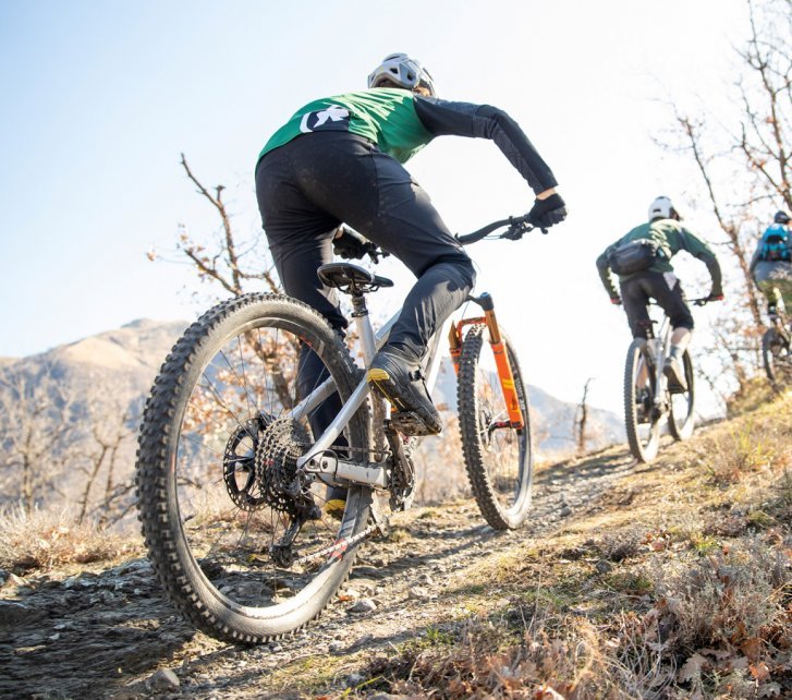 A group of mountain bikers ride up a rocky climb in sunny weather.