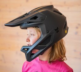 Une fille blonde portant un t-shirt rose met un casque intégral pour le VTT.