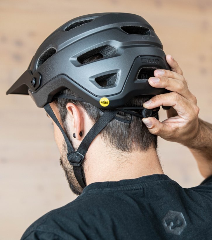 La tête d'un homme aux cheveux bruns portant un casque de vélo, photographiée de dos. Une main actionne la molette de réglage pour ajuster la taille du casque.