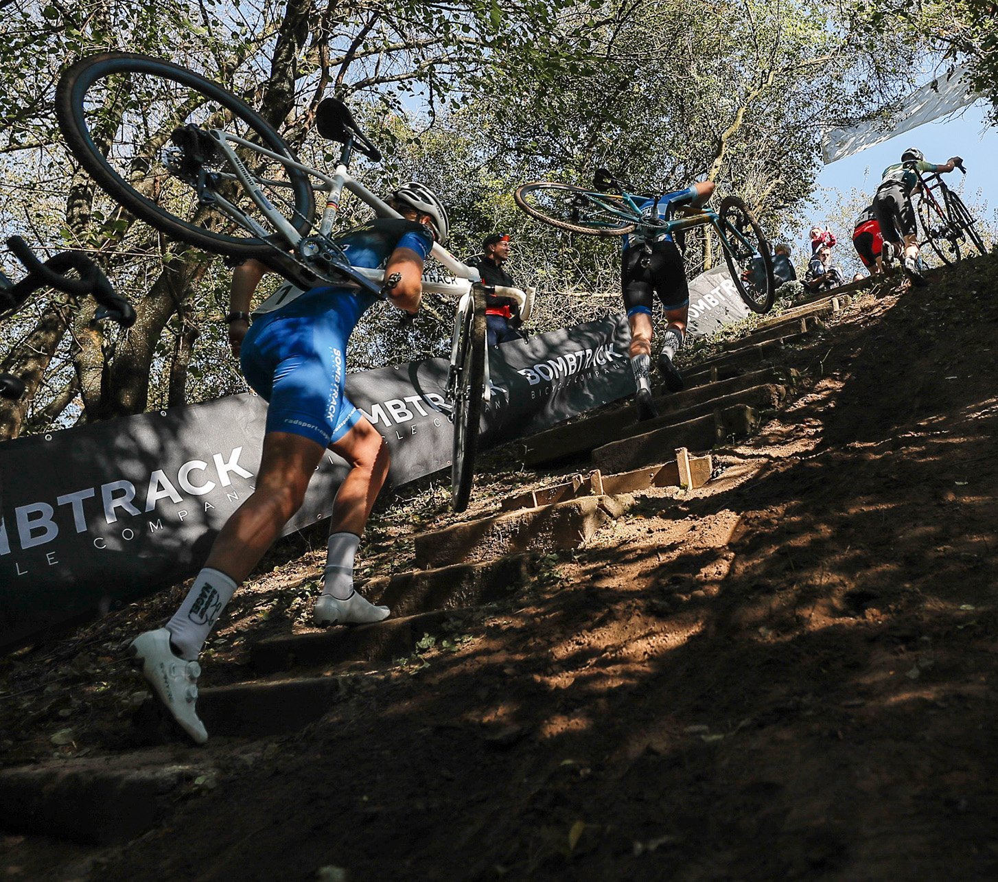 Actionaufnahme vom NRW Cross Cup Cyclocross Event - Cyclocrosser tragen laufend ihre Bikes eine Waldtreppe hoch.