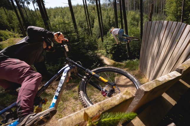 Action shot of two bc employees riding a wallride on their mountain bikes in a bike park.