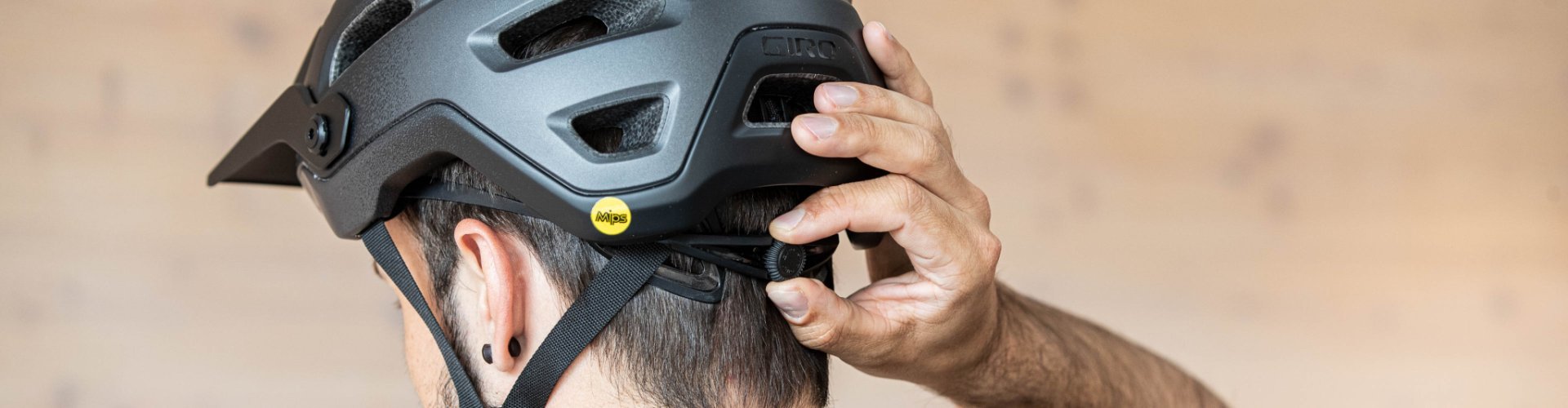 La tête d'un homme aux cheveux bruns portant un casque de vélo, photographiée de dos. Une main ajuste la molette pour modifier l'ajustement du casque.