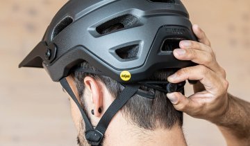 Kopf eines dunkelhaarigen Mannes mit Fahrradhelm, von hinten aufgenommen. Eine Hand bedient den Verstellknopf zur Weitenanpassung des Fahrradhelms