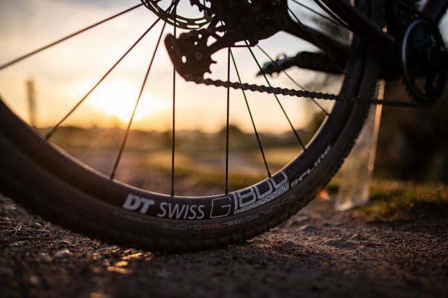 Scenic close-up of a DT Swiss gravel wheel on firm gravel at sunset.