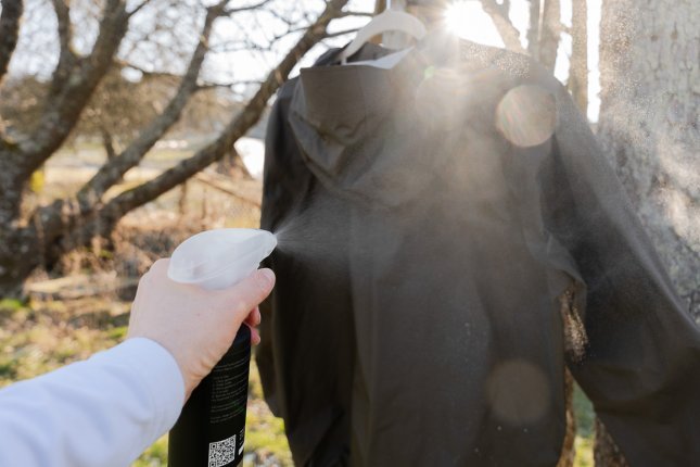 Une veste hardshell est accrochée sur un cintre à un arbre. Le brouillard du spray d’imprégnation est visible en contre-jour.