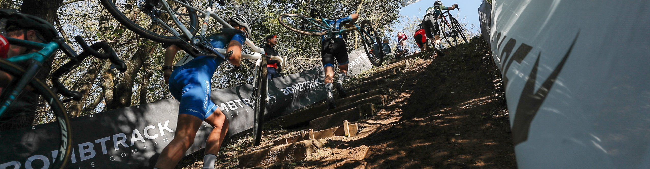 Actionaufnahme vom NRW Cross Cup Cyclocross Event - Cyclocrosser tragen laufend ihre Bikes eine Waldtreppe hoch.