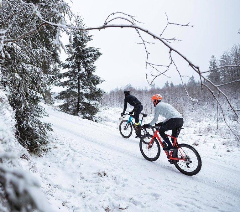 Zwei Gravel Biker fahren durch einen schneebedeckten Wald