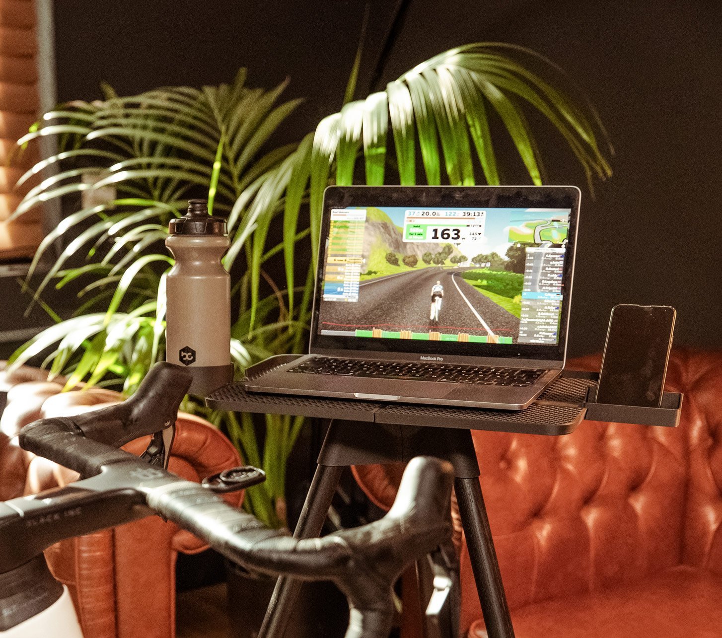 Ein Macbook steht auf einem tons Laptopständer. Auf dem Bildschirm ist eine Zwift Fahrsimulation zu sehen.