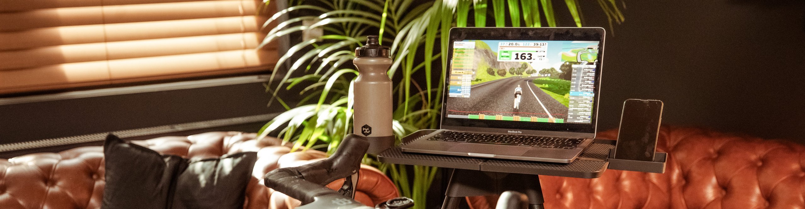 Ein Macbook steht auf einem tons Laptopständer. Auf dem Bildschirm ist eine Zwift Fahrsimulation zu sehen.