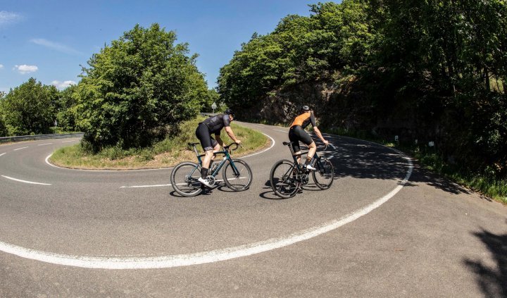 Zwei Rennradfahrer, beide auf Specialized Tarmac SL7 Bikes, passieren bergauf eine Serpentine.