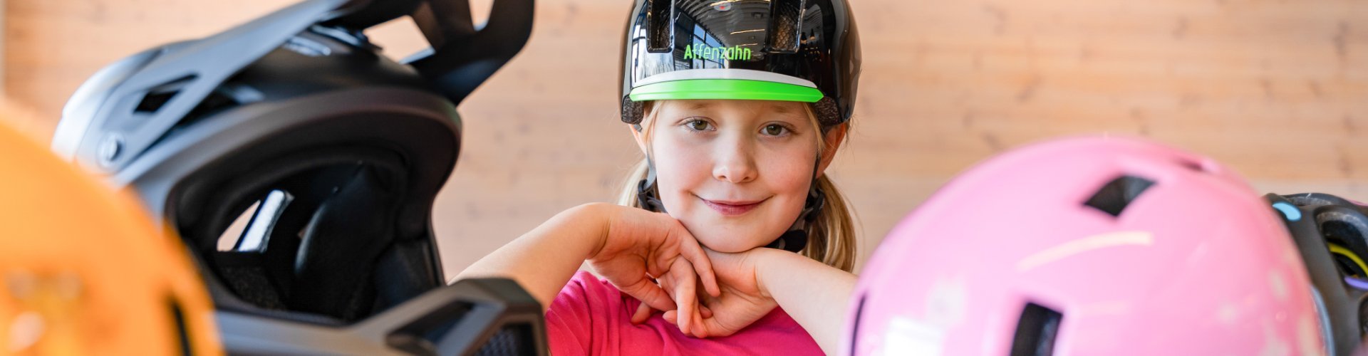 Charlotte trägt einen Fahrradhelm von Affenzahn und schaut zwischen vielen, nur teilweise sichtbaren Helmen hervor.