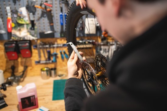 Over-the-shoulder view of a mechanic: His hand holds a disc brake alignment tool to the brake disc of an MTB wheel.