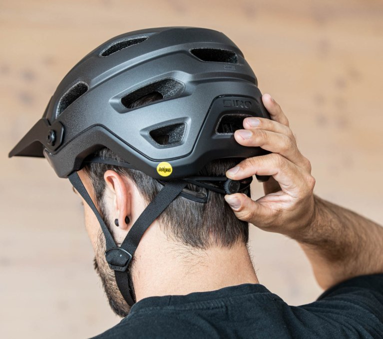 Cabeza de un hombre de cabello oscuro con casco de bicicleta, visto desde atrás. Una mano ajusta el dial para modificar el tamaño del casco.