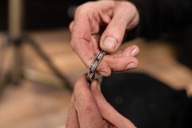 Closeup Foto: Ein Mechaniker hält eine frisch gewachste Fahrradkette in seinen Händen. Die Kette ist sauber, man kann kleine Wachkrümel erkennen.