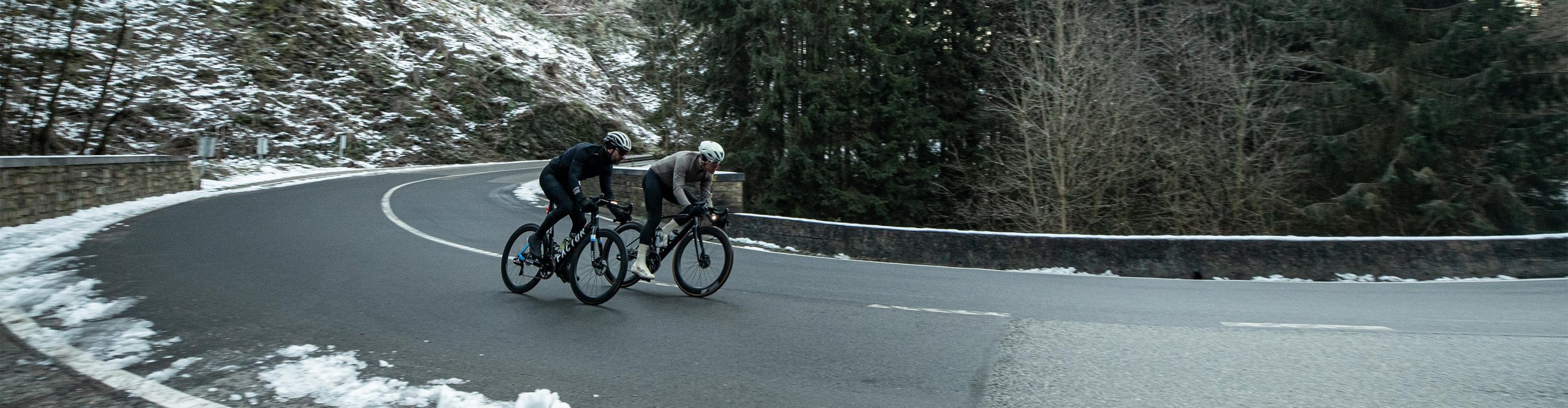 Zwei Rennradfahrer fahren eine große Straßenkurve inmitten einer winterlichen Szenerie