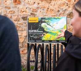 Deux personnes, partiellement coupées et floues au premier plan, se tiennent devant un présentoir avec plusieurs roues gravel suspendues côte à côte. Le présentoir affiche le message Put an end to gravel nightmares.