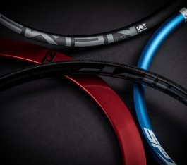 Four bicycle rims in black, red, and blue are lying on a dark surface.