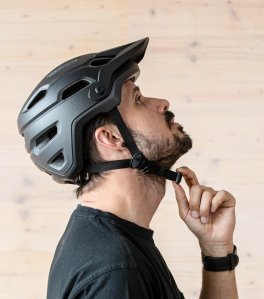 Un homme avec un casque de vélo de profil. Le casque est correctement ajusté, la personne regarde vers le plafond, montrant à quel point la jugulaire est serrée.