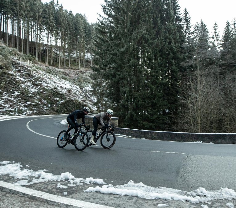 Zwei Rennradfahrer fahren eine große Straßenkurve inmitten einer winterlichen Szenerie