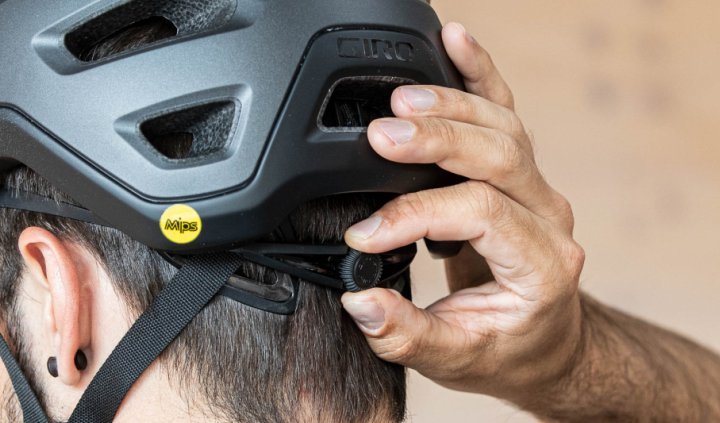 La tête d'un homme aux cheveux bruns portant un casque de vélo, photographiée de dos. Une main ajuste la molette pour modifier l'ajustement du casque.