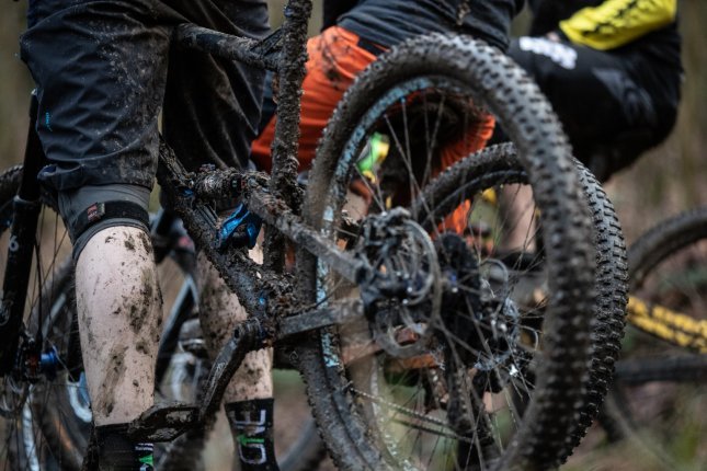 Un short de VTT très sale et un mollet d'homme très sale à côté d'un VTT très sale.