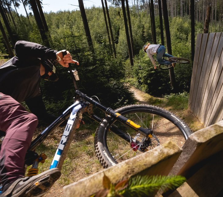 Action shot of two bc employees riding a wallride on their mountain bikes in a bike park.