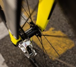 Close-up of a Black Inc front hub with a Ceramicspeed logo in a yellow-black carbon fork with a silver-colored brake caliper.