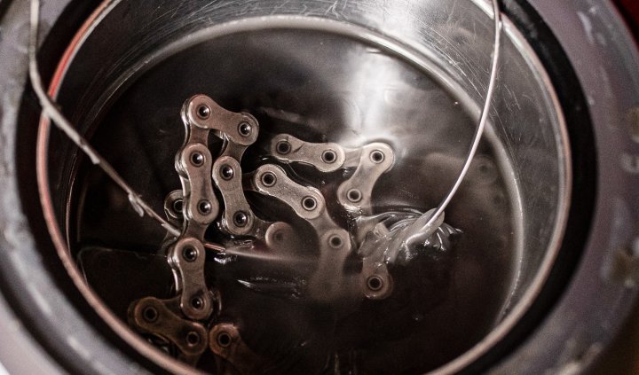 Une chaîne de vélo repose dans une casserole avec de la cire pour chaîne grise et transparente qui refroidit.