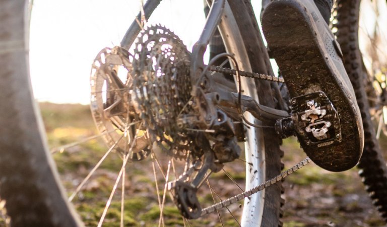 Photo d'action : Un VTT passe devant la caméra. Dans le cadre, on ne voit que les roues avec des pneus à gros crampons en contre-jour. La mise au point est sur le pied du cycliste et sur le OneUp Clip Pedal.