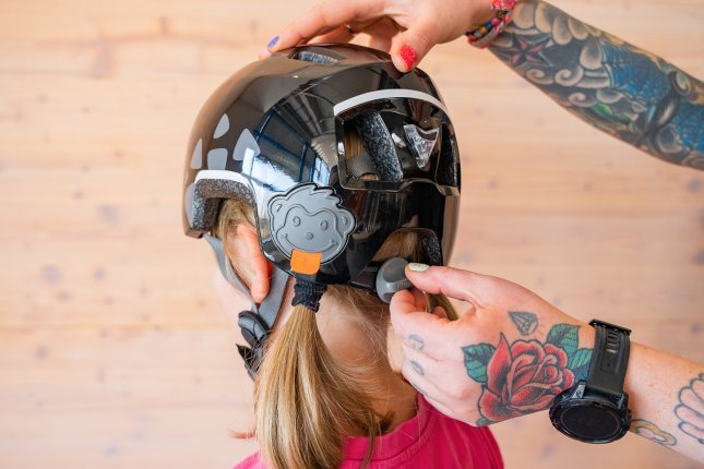 Les mains tatouées d’une mère ajustent la taille du casque de vélo sur la tête d’un enfant à l’aide du réglage de taille.